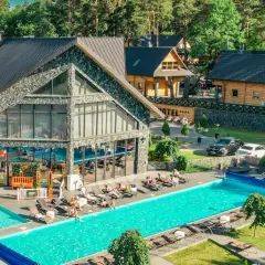 Nowoczesny kompleks hotelowy z basenami i leżakami, otoczony lasem.