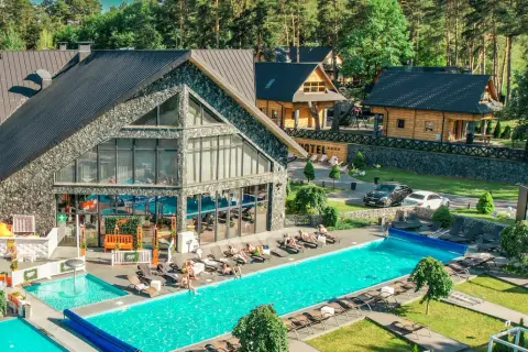 Nowoczesny kompleks hotelowy z basenami i leżakami, otoczony lasem.
