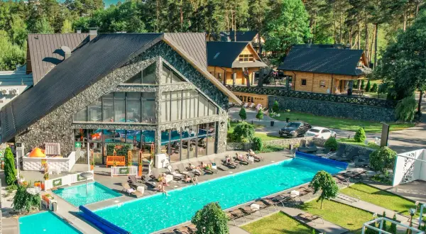 Nowoczesny kompleks hotelowy z basenami i leżakami, otoczony lasem.