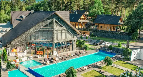Nowoczesny kompleks hotelowy z basenami i leżakami, otoczony lasem.